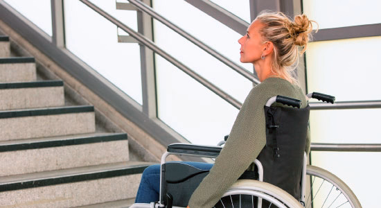 Woman in a wheelchair at the bottom of a staircase with no ramp access