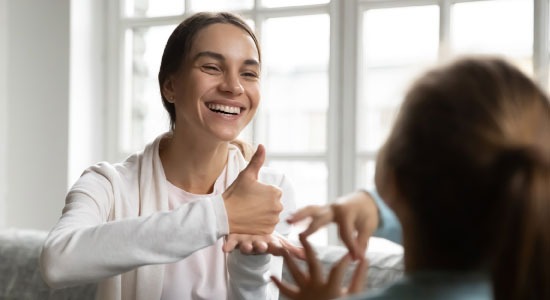 Woman smiling and signing with a young girl at home