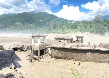 Buildings buried to their roofs in flood silt beside a Nepali river.