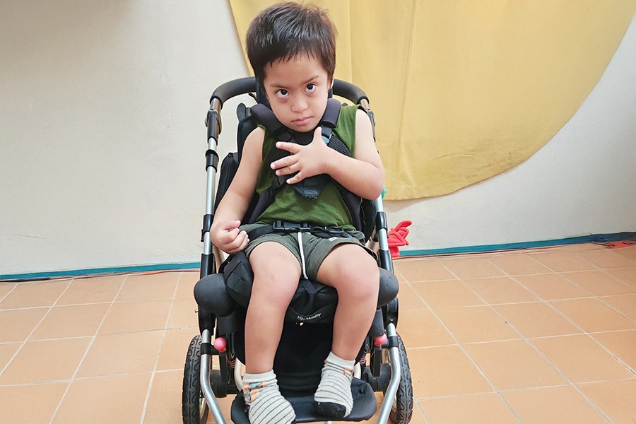 Enoch, age four, sitting in his specialised wheelchair buggy in Tuvalu and looking at the camera