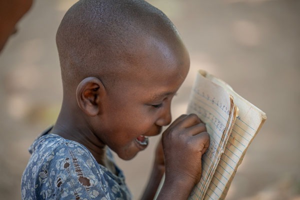 Faith from Uganda sitting at her school desk, unable to see her work due to blinding cataracts